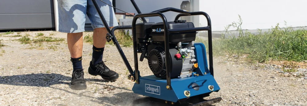 Person verdichtet Schotter mit einer Rüttelplatte.